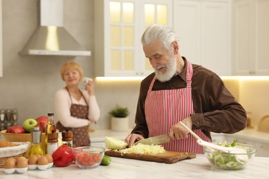 Senior woman looking at her husband cooking in kitchen, selective focus