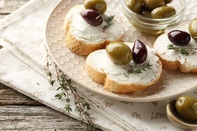 Photo of Delicious sandwiches with marinated olives, cream cheese and thyme on wooden table, closeup