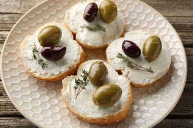 Photo of Delicious sandwiches with marinated olives, cream cheese and thyme on wooden table, above view