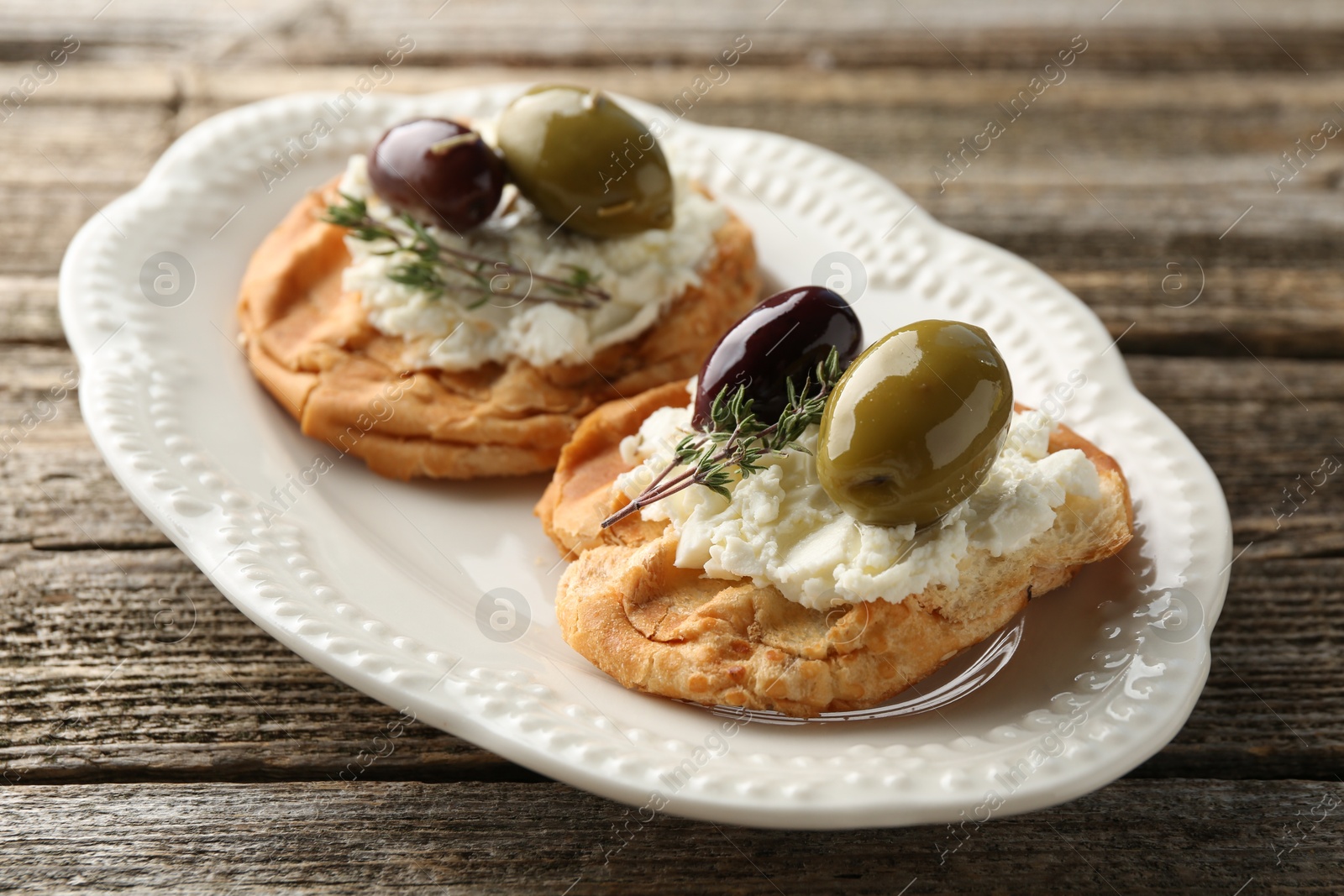 Photo of Delicious sandwiches with marinated olives, cream cheese and thyme on wooden table, closeup