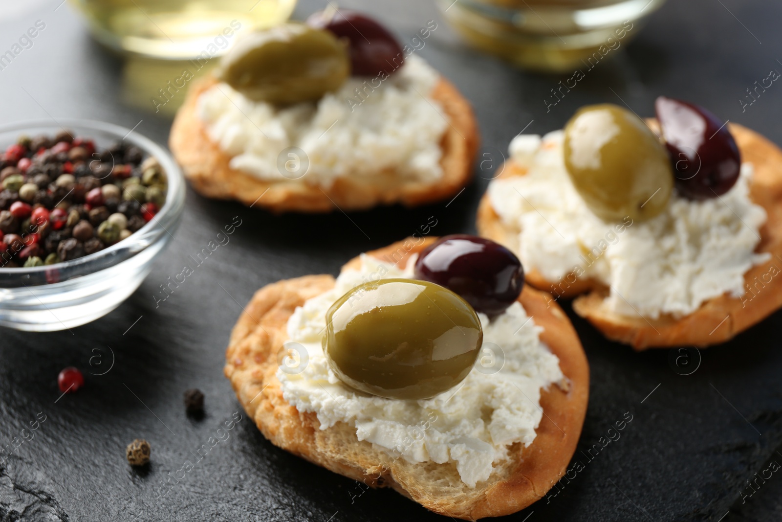 Photo of Delicious sandwiches with marinated olives, cream cheese and peppercorns on dark table, closeup