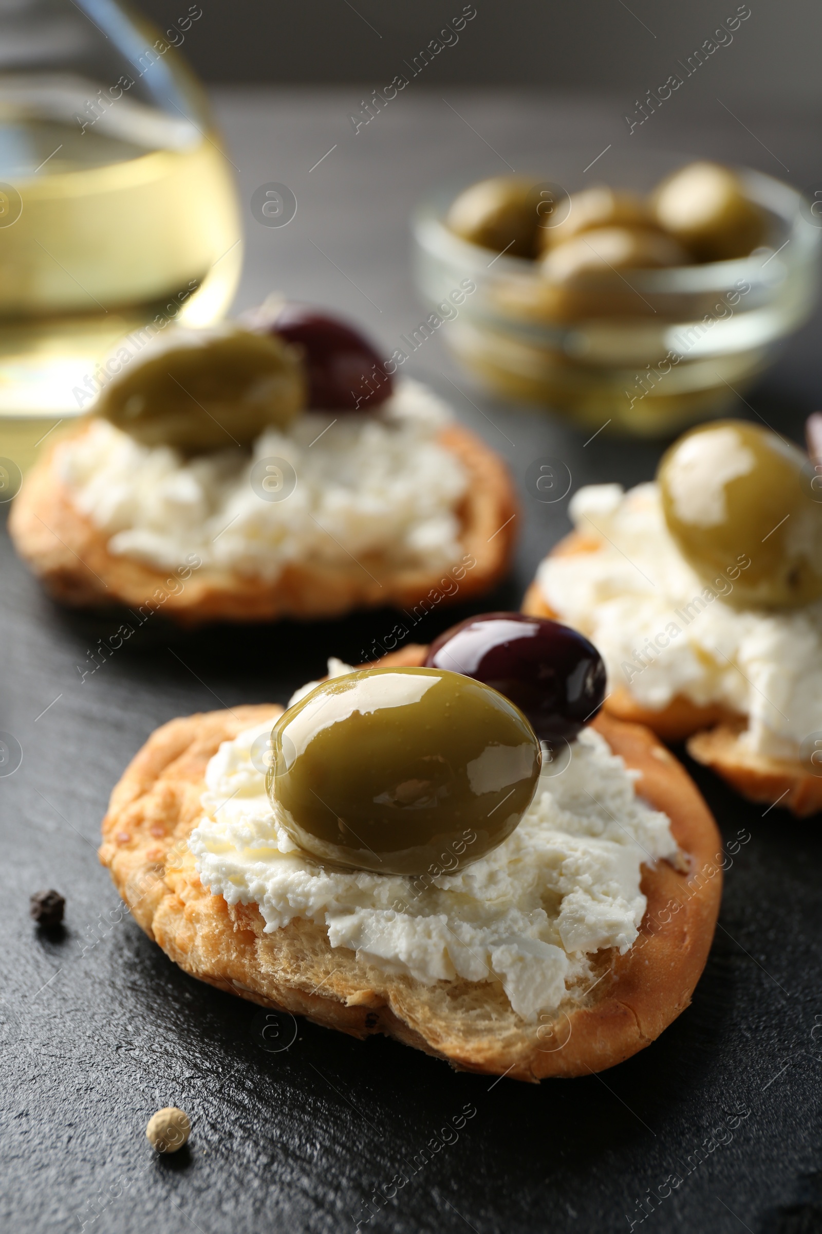 Photo of Delicious sandwiches with marinated olives, cream cheese and peppercorns on dark table, closeup