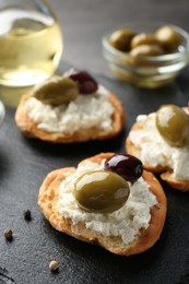 Photo of Delicious sandwiches with marinated olives, cream cheese and peppercorns on dark table, closeup