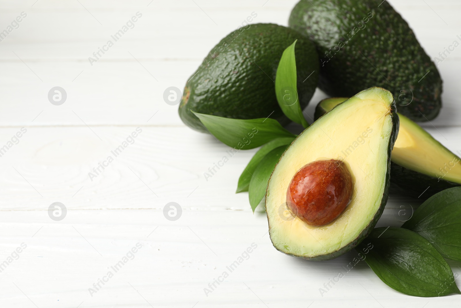 Photo of Whole and cut avocados on white wooden table, closeup. Space for text