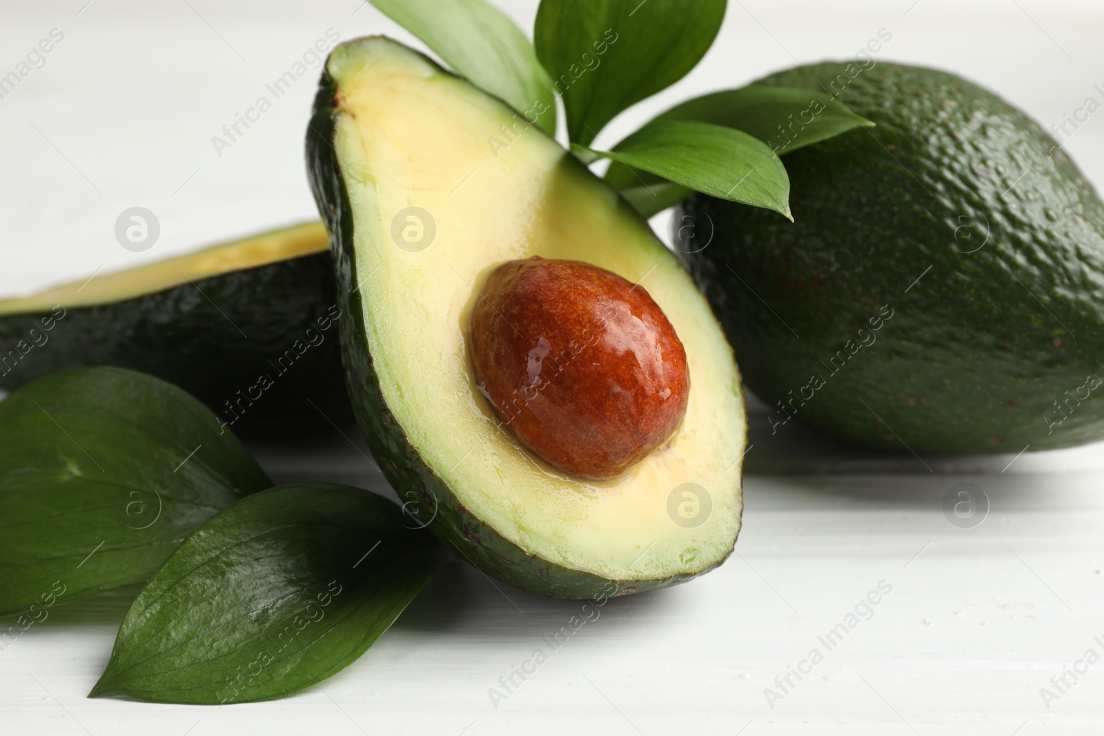 Photo of Whole and cut avocados on white wooden table, closeup