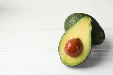 Photo of Whole and cut avocados on white wooden table, closeup. Space for text