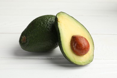 Photo of Whole and cut avocados on white wooden table, closeup