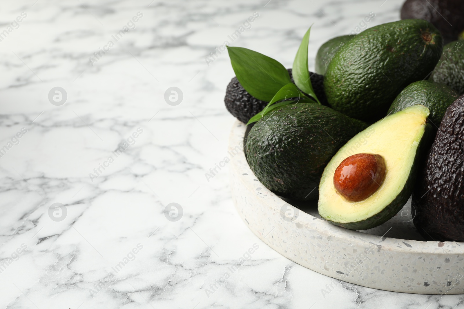 Photo of Whole and cut avocados on white marble table, closeup. Space for text