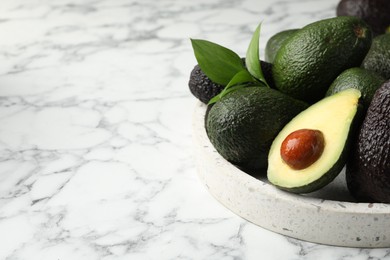 Photo of Whole and cut avocados on white marble table, closeup. Space for text