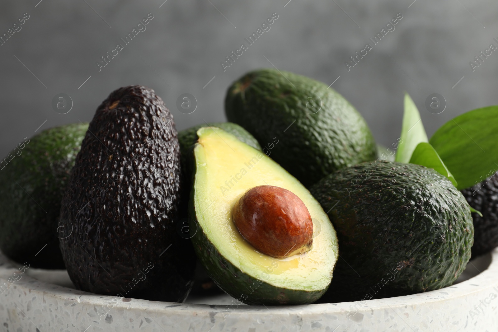 Photo of Whole and cut avocados on plate against blurred grey background, closeup