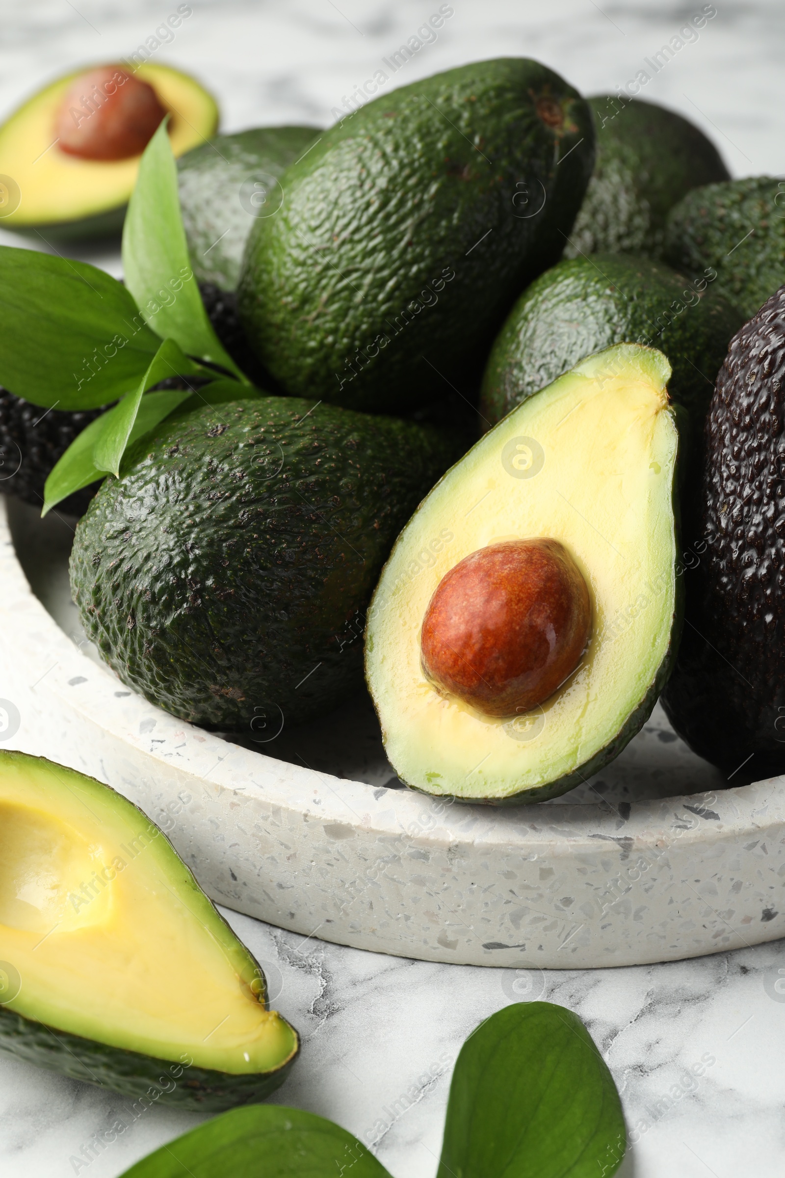 Photo of Whole and cut avocados on white marble table, closeup