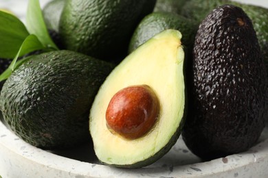 Photo of Whole and cut avocados on plate, closeup