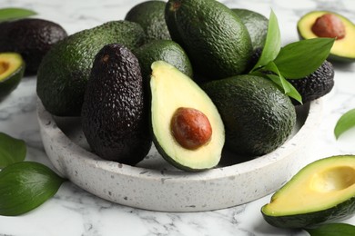 Photo of Whole and cut avocados on white marble table, closeup