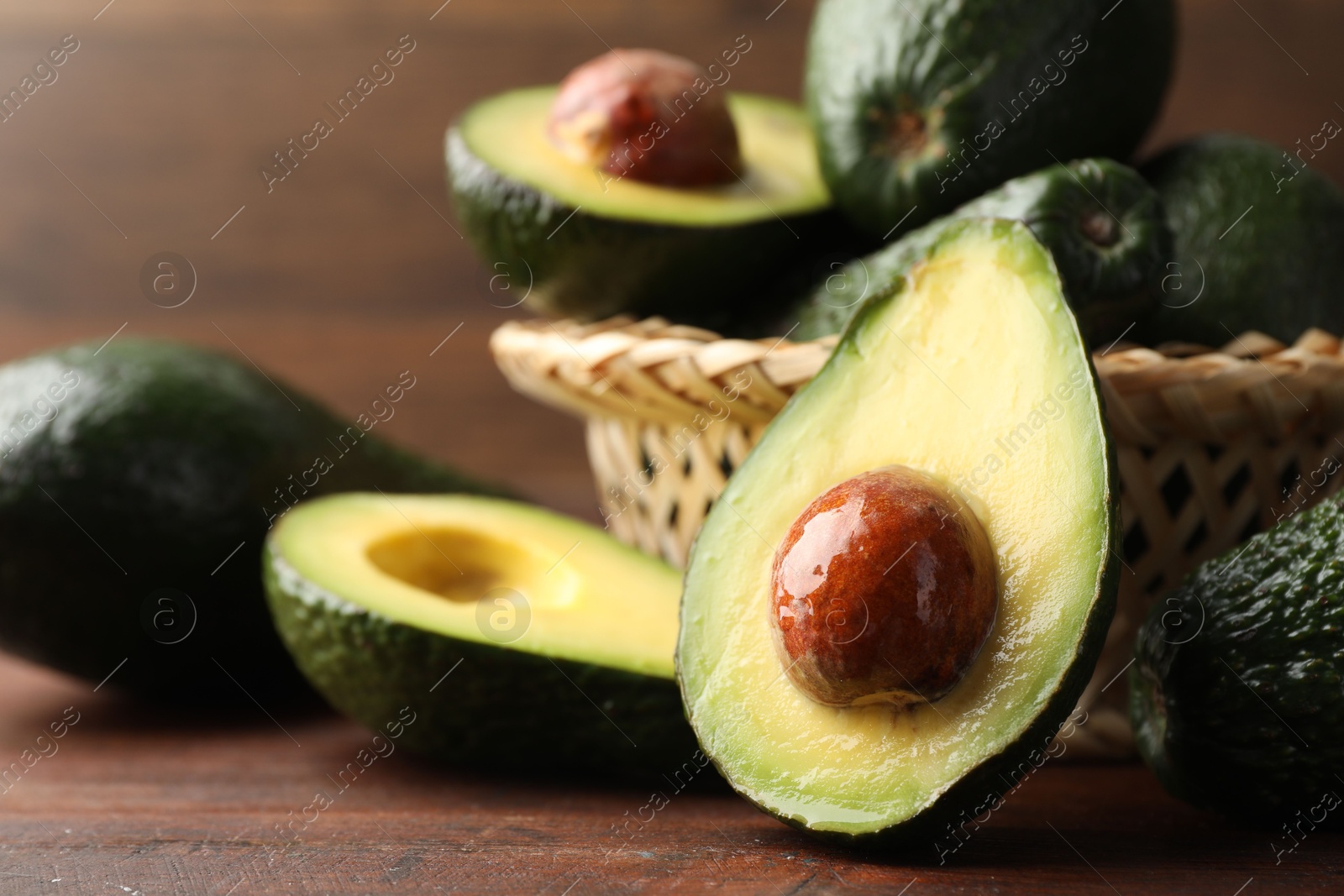 Photo of Whole and cut avocados on wooden table, closeup