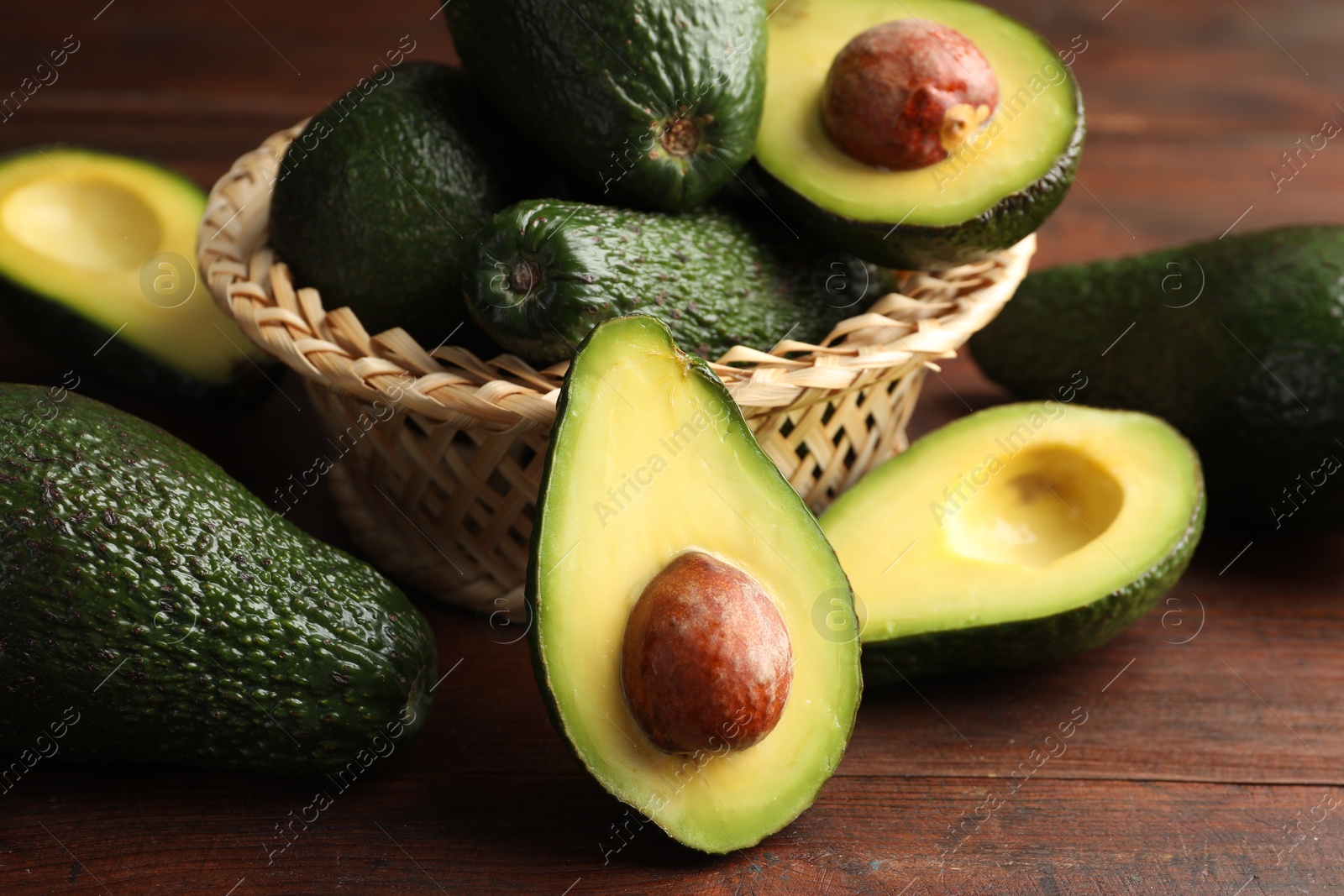 Photo of Whole and cut avocados on wooden table, closeup