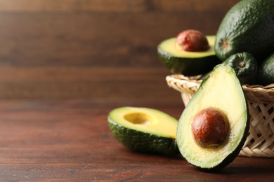 Photo of Whole and cut avocados on wooden table, closeup. Space for text