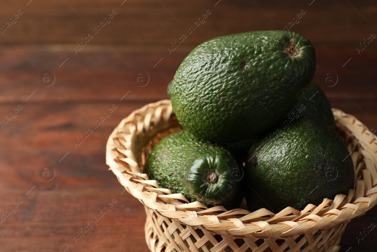 Photo of Whole avocados in wicker basket on wooden table, closeup. Space for text