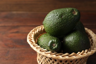 Photo of Whole avocados in wicker basket on wooden table, closeup. Space for text