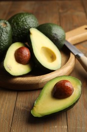 Photo of Whole and cut avocados on wooden table, closeup