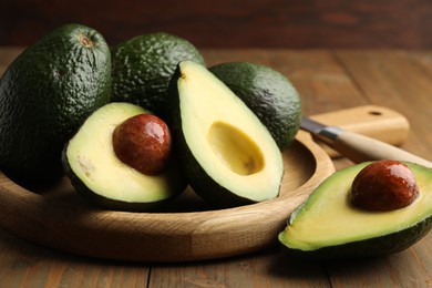 Photo of Whole and cut avocados on wooden table, closeup