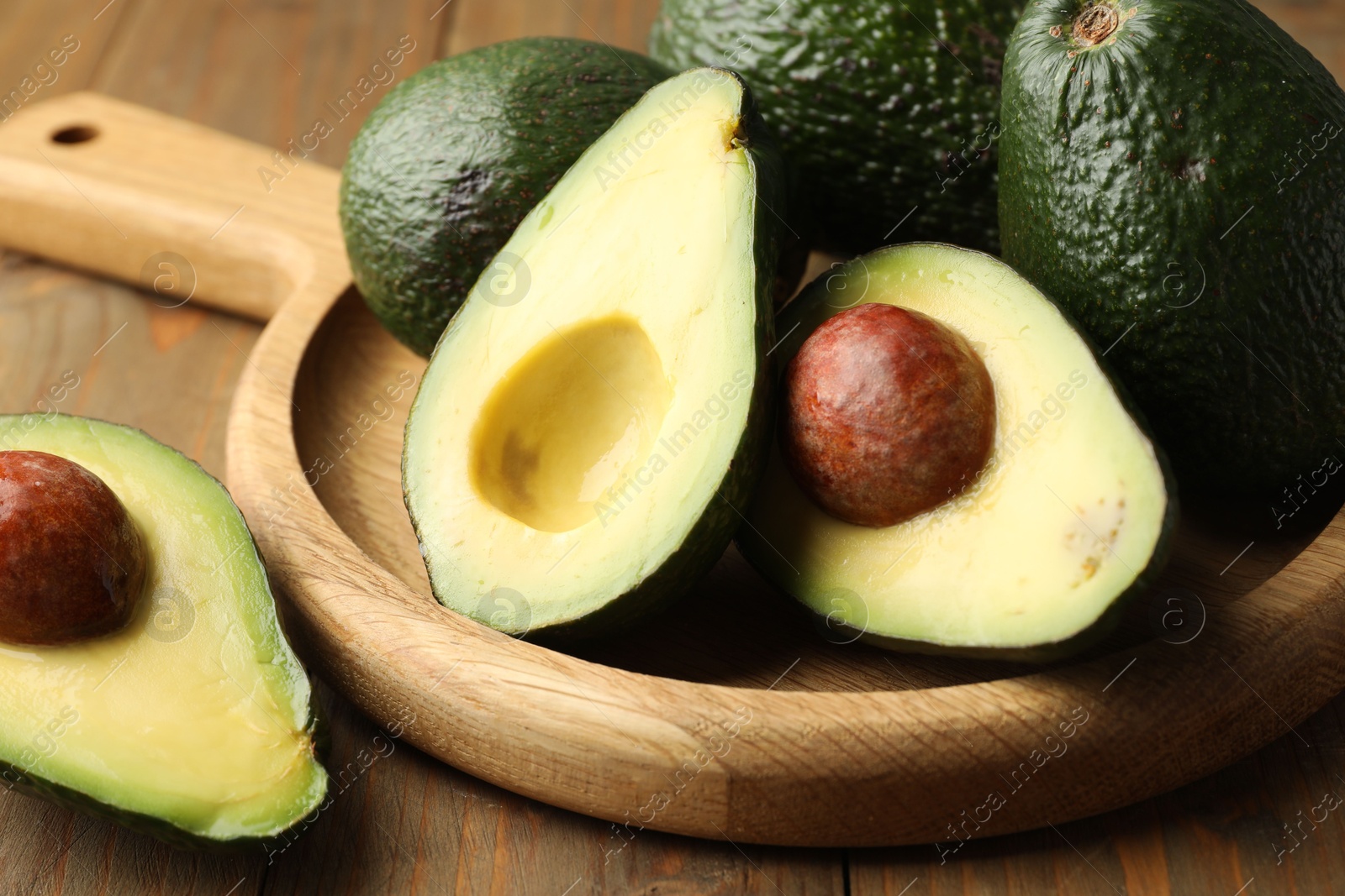 Photo of Whole and cut avocados on wooden table, closeup