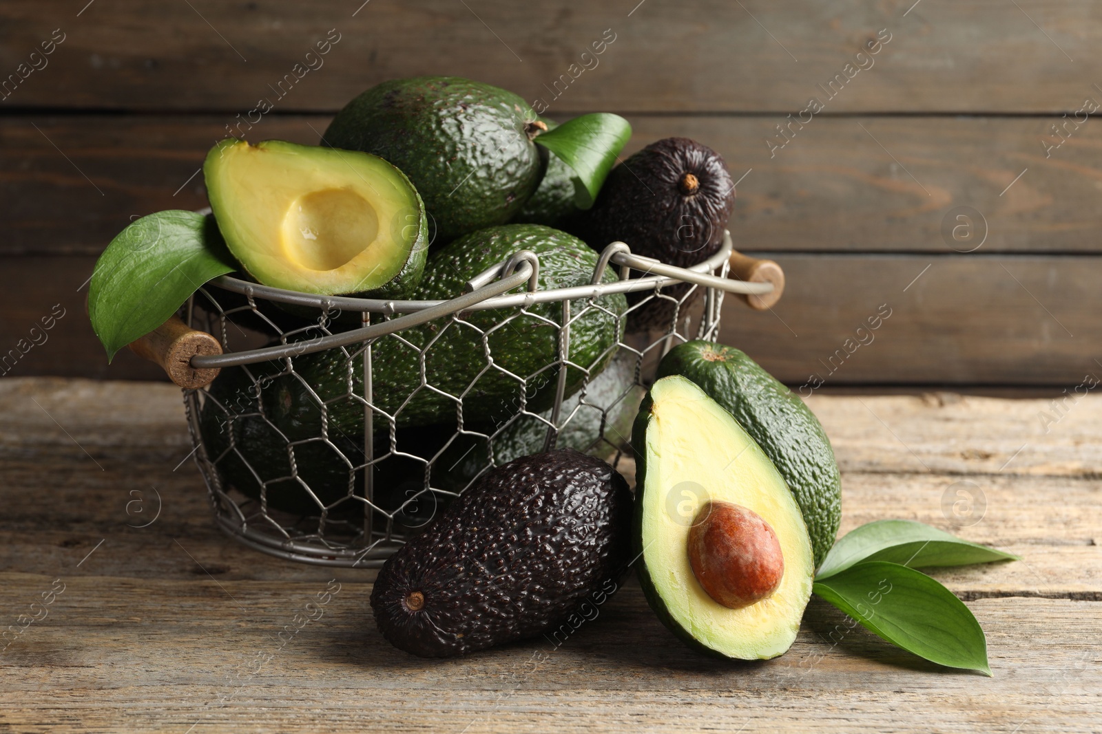 Photo of Whole and cut avocados on wooden table, closeup