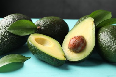 Photo of Whole and cut avocados on light blue wooden table, closeup