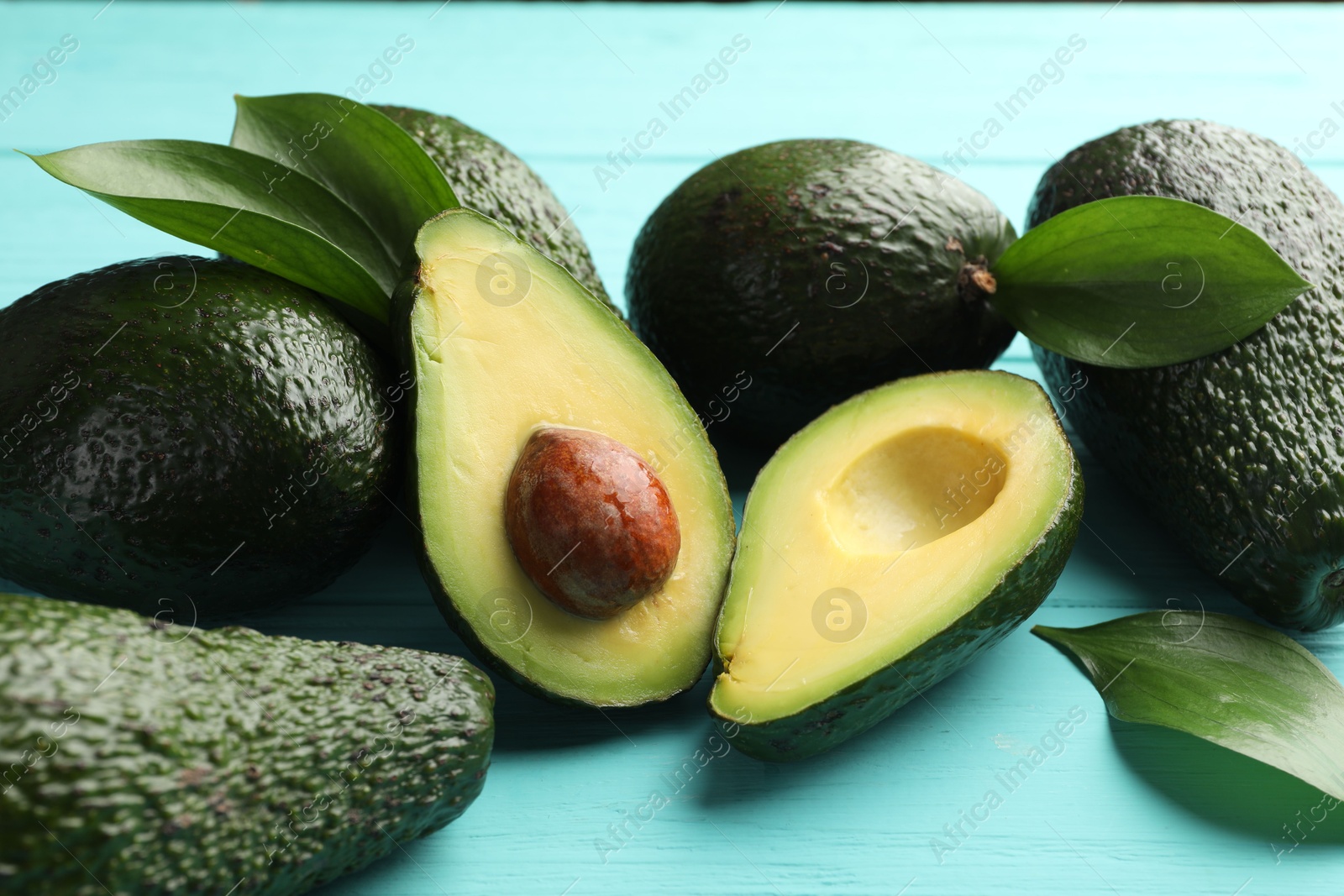 Photo of Whole and cut avocados on light blue wooden table, closeup