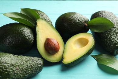 Photo of Whole and cut avocados on light blue wooden table, closeup