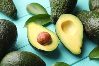 Photo of Whole and cut avocados on light blue wooden table, closeup