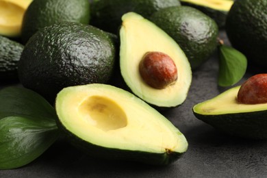 Photo of Whole and cut avocados on grey textured table, closeup