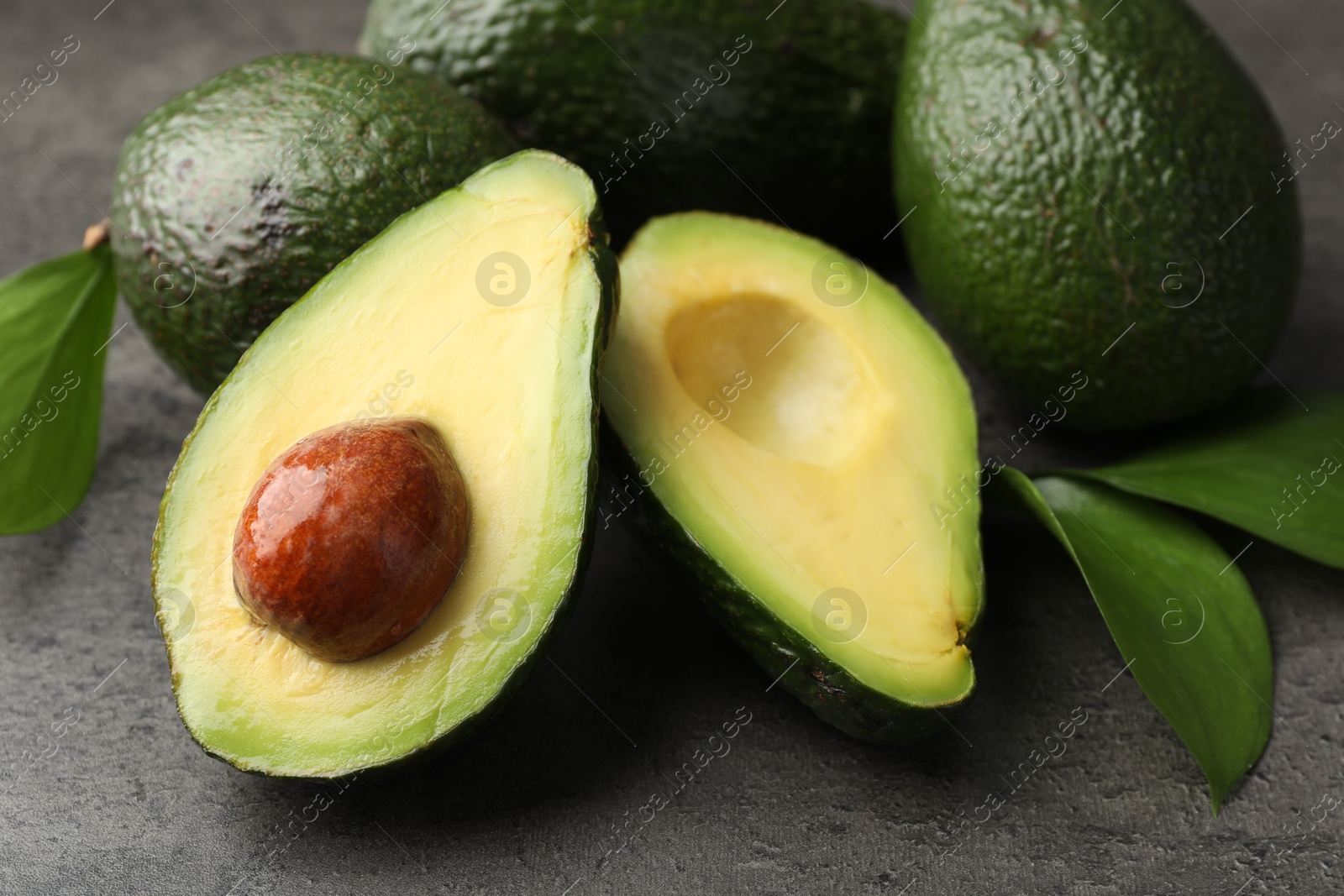 Photo of Whole and cut avocados on grey textured table, closeup