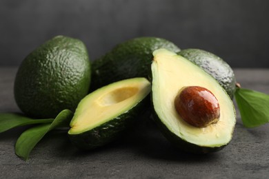 Photo of Whole and cut avocados on grey textured table, closeup