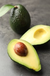 Photo of Whole and cut avocados on grey textured table, closeup