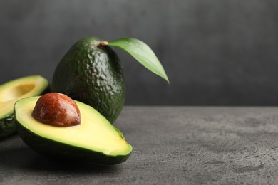 Photo of Whole and cut avocados on grey textured table, closeup. Space for text