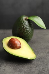 Photo of Whole and cut avocados on grey textured table, closeup