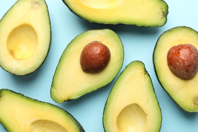 Photo of Halves of fresh avocados on light blue background, flat lay