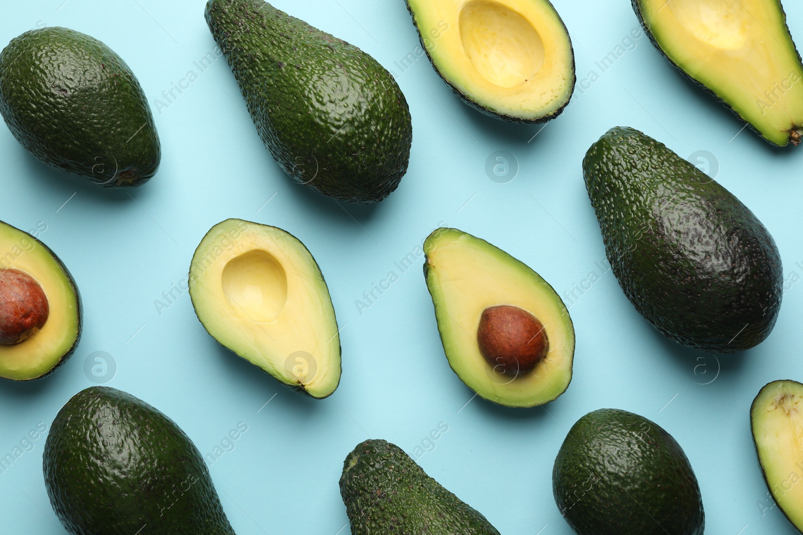 Photo of Whole and cut avocados on light blue background, flat lay