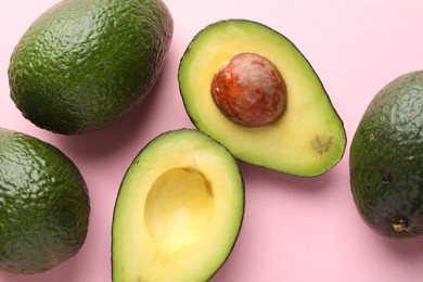 Photo of Whole and cut avocados on pink background, flat lay