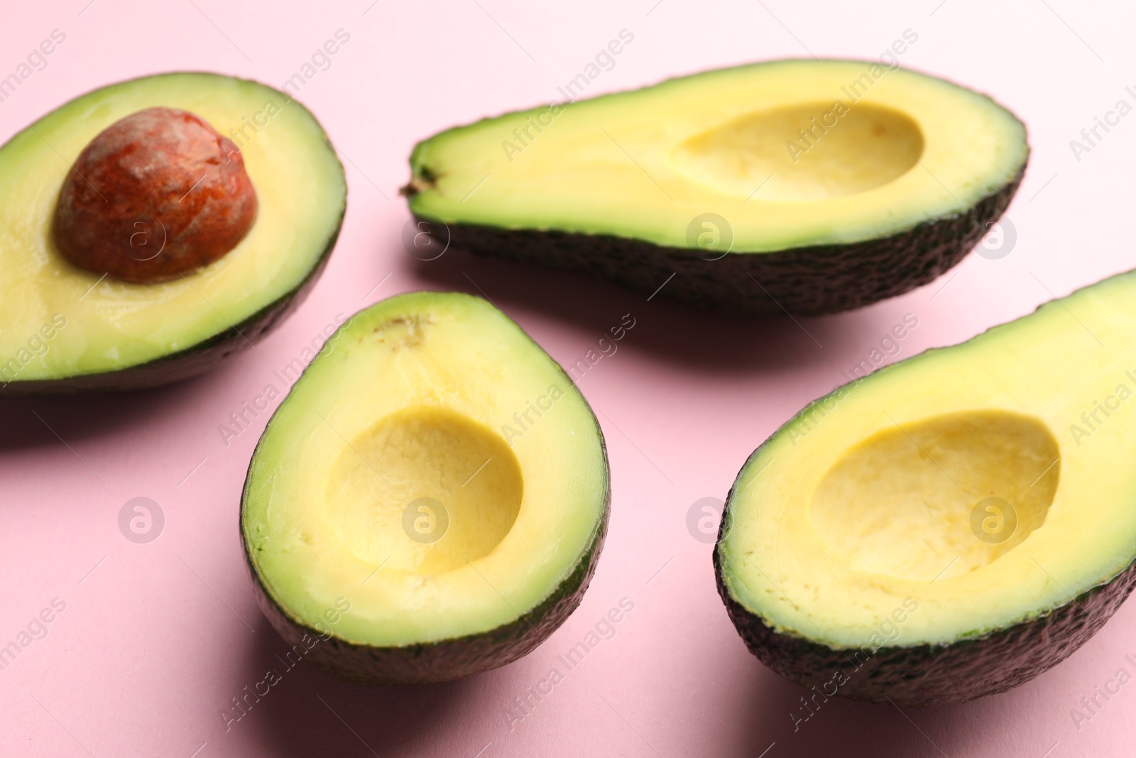 Photo of Halves of fresh avocados on pink background, closeup