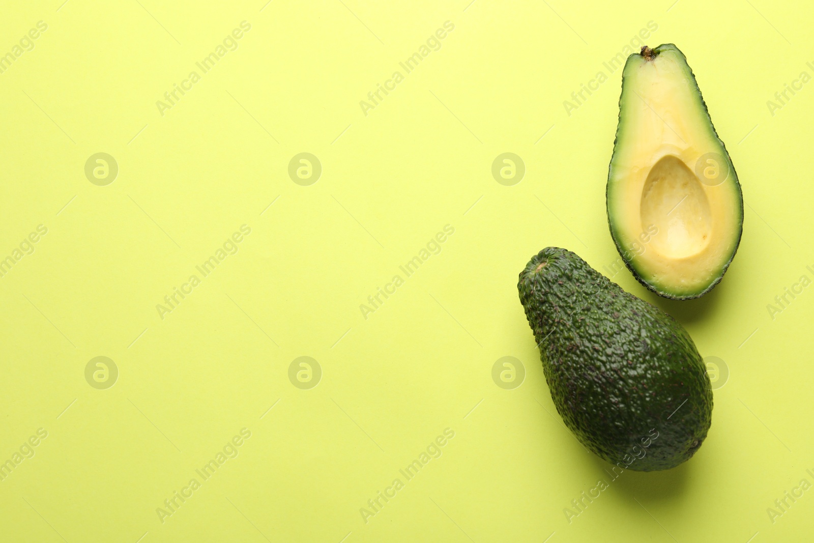 Photo of Whole and cut avocados on light green background, flat lay. Space for text