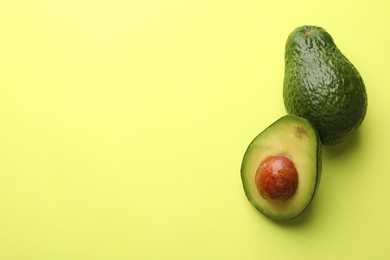 Photo of Whole and cut avocados on light green background, flat lay. Space for text