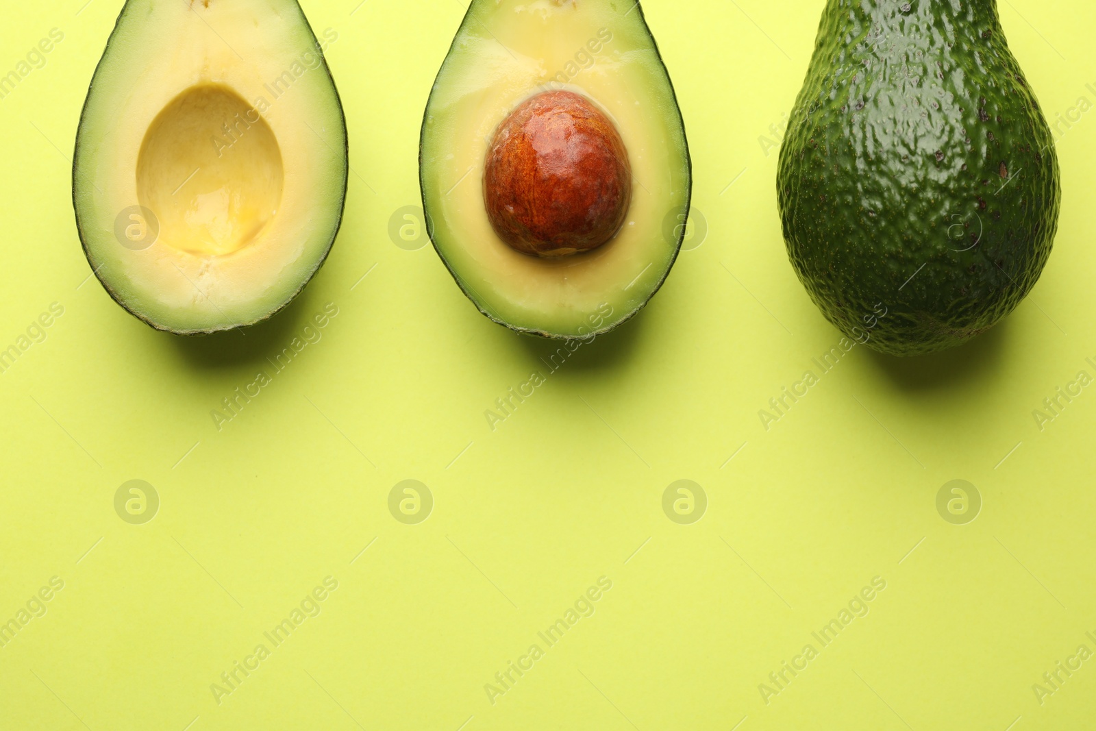 Photo of Whole and cut avocados on light green background, flat lay. Space for text