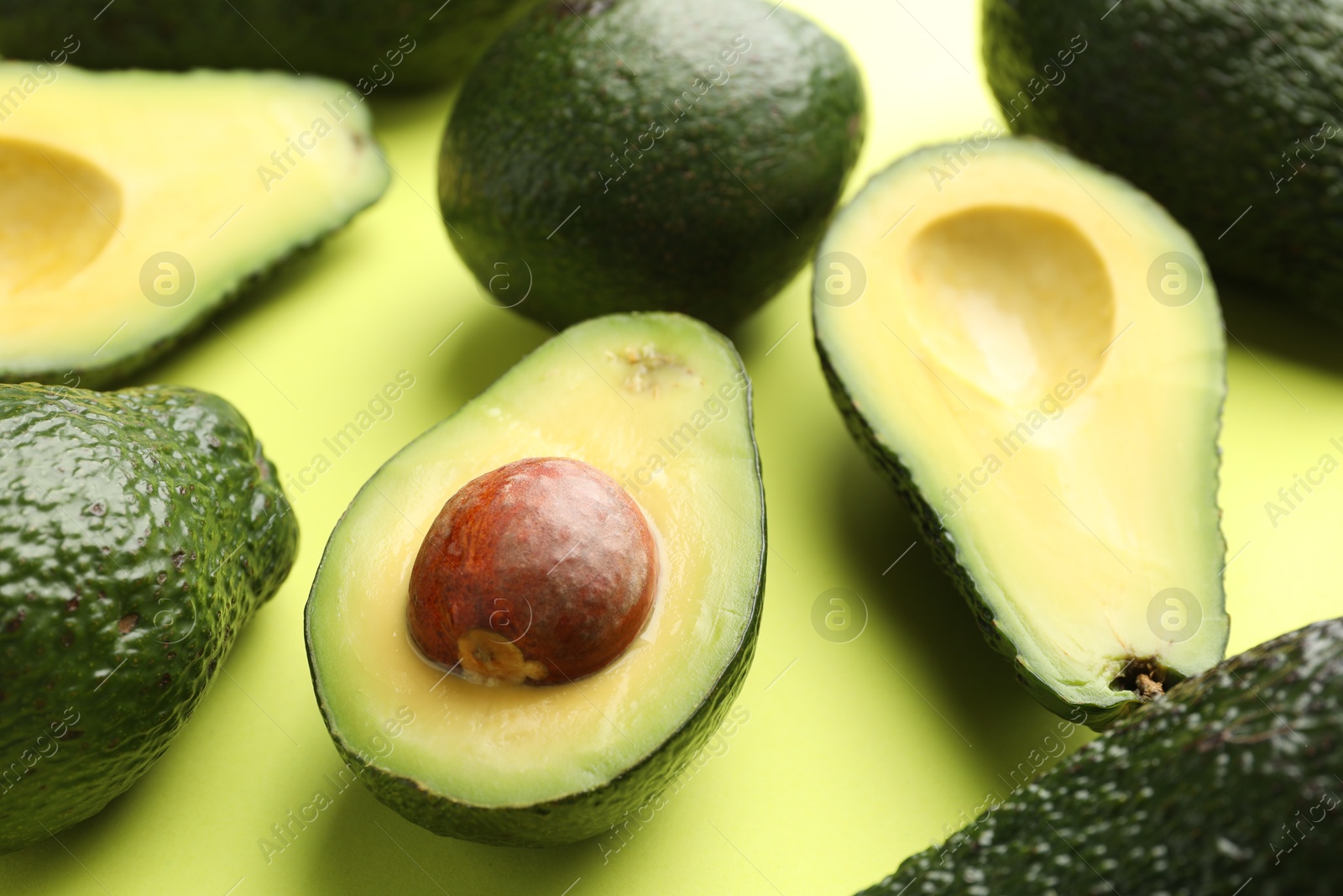 Photo of Whole and cut avocados on light green background, closeup