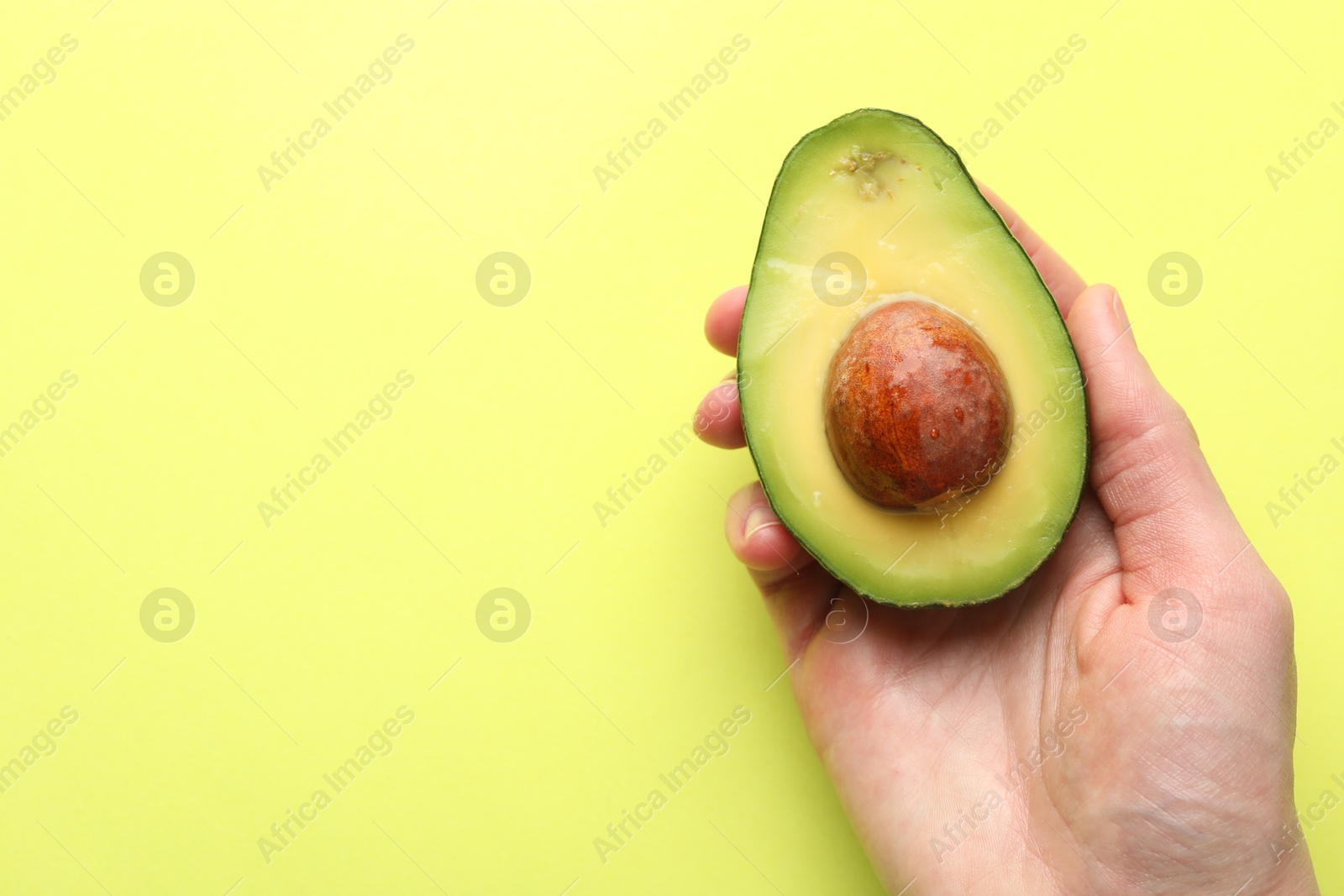 Photo of Woman with half of fresh avocado on light green background, closeup. Space for text