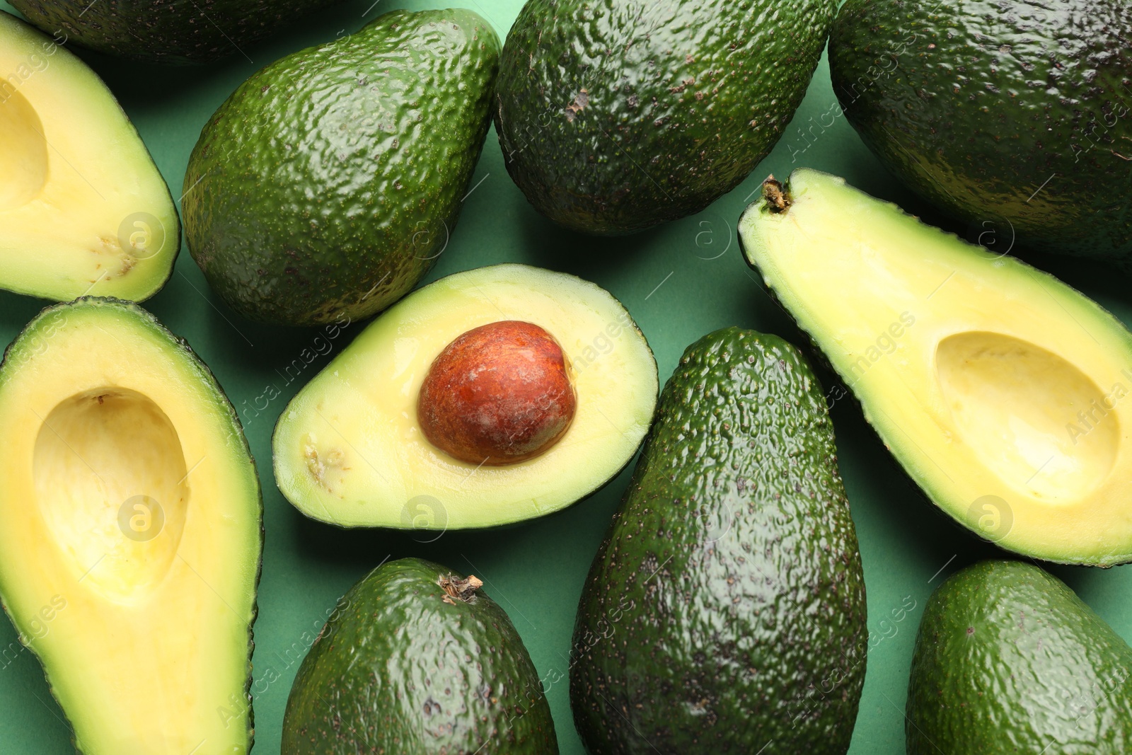 Photo of Whole and cut avocados on green background, flat lay