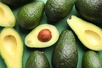 Photo of Whole and cut avocados on green background, flat lay