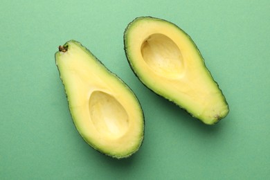 Photo of Halves of fresh avocado on green background, flat lay