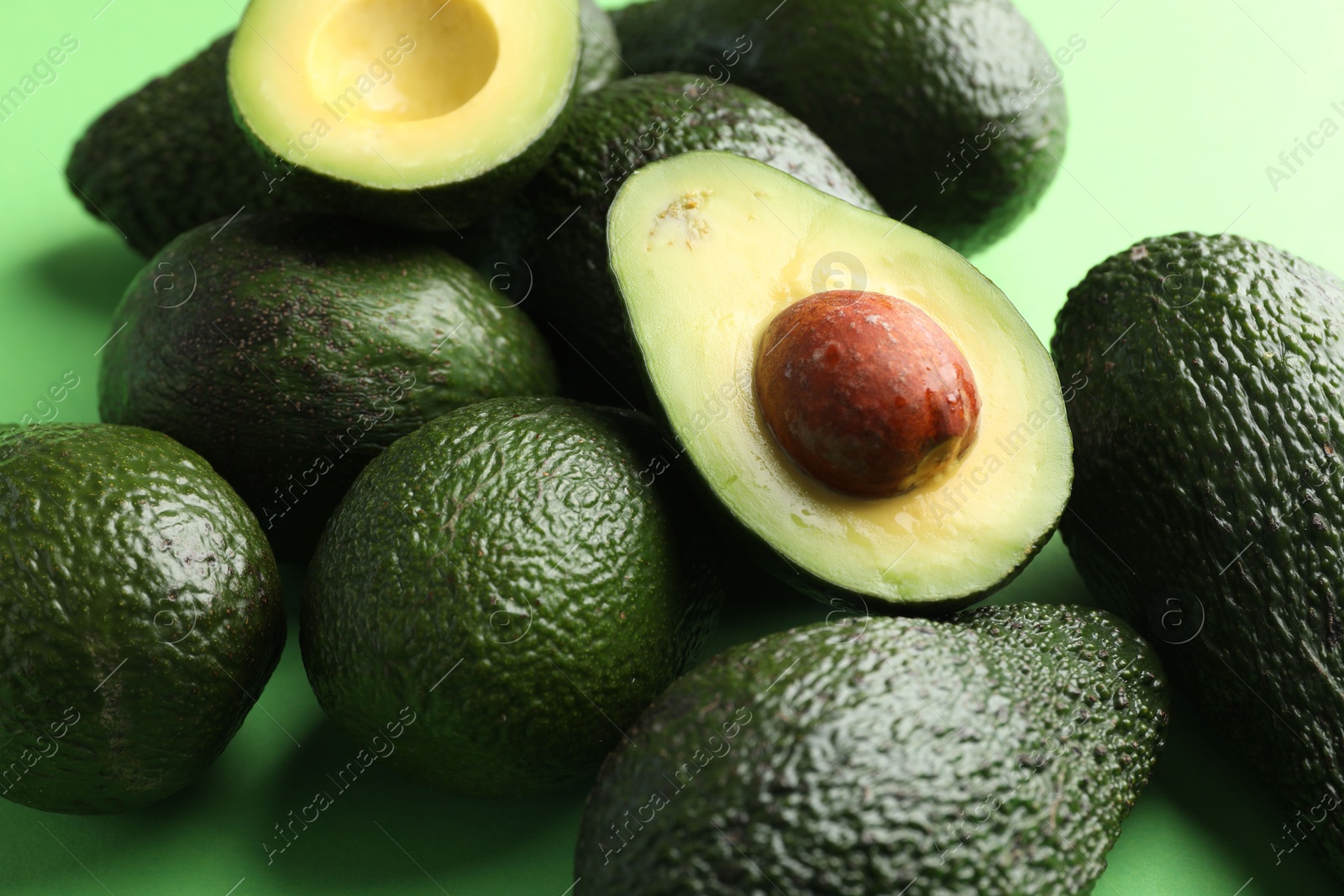 Photo of Whole and cut avocados on green background, closeup