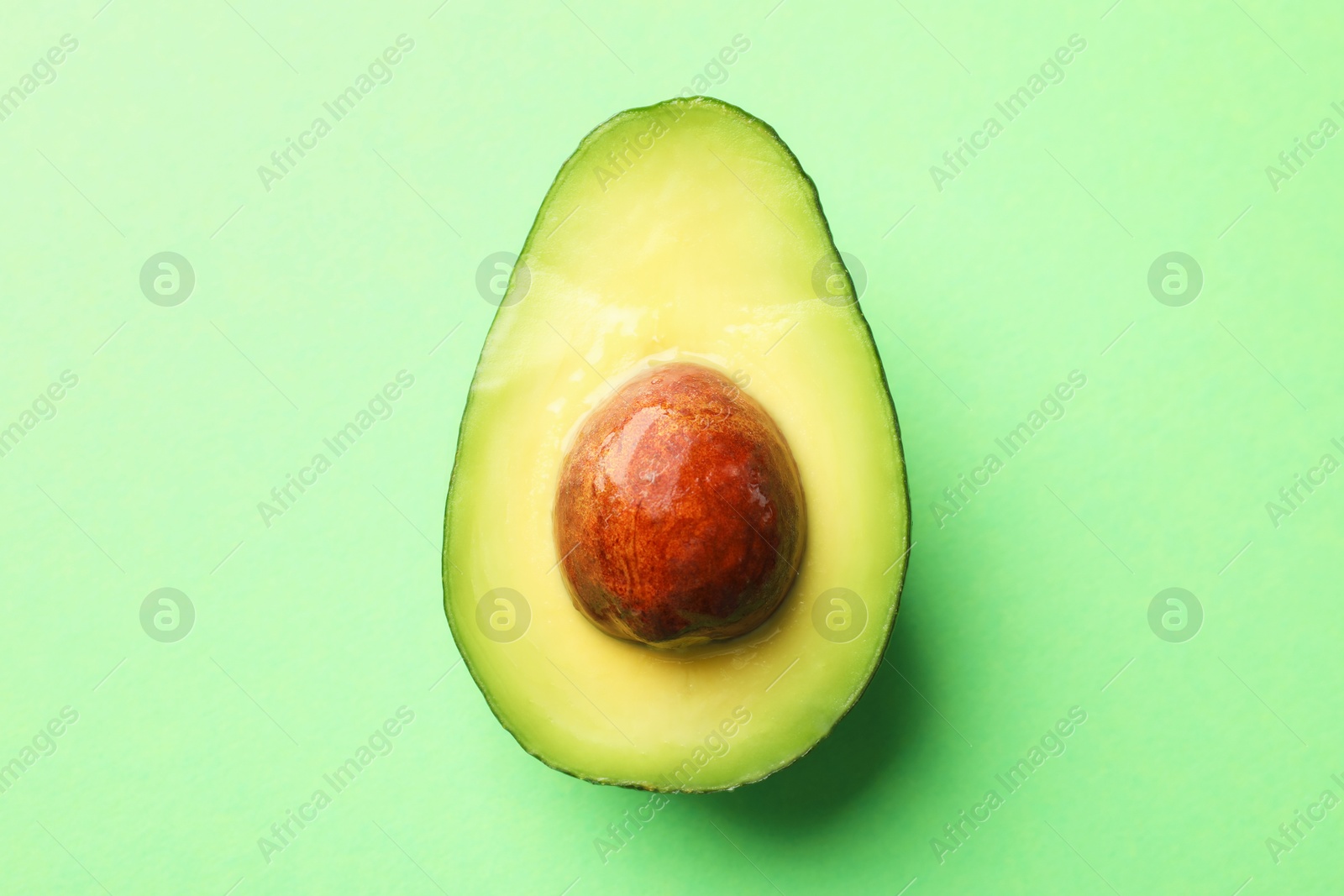 Photo of Half of fresh avocado on green background, top view